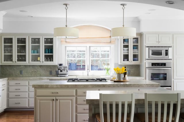 kitchen with glass insert cabinets, light countertops, appliances with stainless steel finishes, crown molding, and backsplash