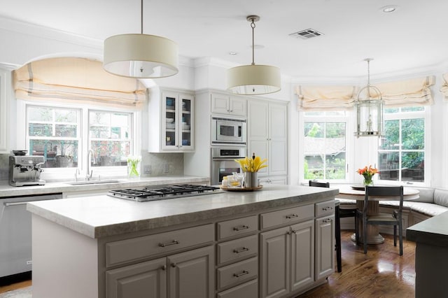 kitchen with glass insert cabinets, a sink, appliances with stainless steel finishes, dark wood finished floors, and a kitchen island