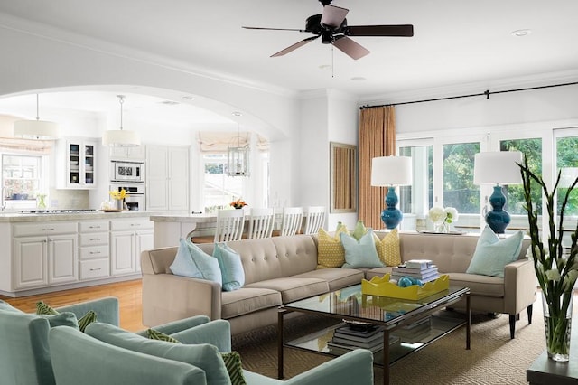 living area with arched walkways, ornamental molding, a ceiling fan, recessed lighting, and light wood-style flooring