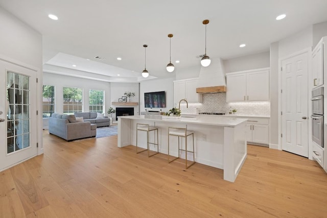 113 Oak Plaza Dr, Georgetown, TX 78628 - kitchen with light wood-style flooring, white cabinetry, custom exhaust hood, light countertops, and decorative backsplash