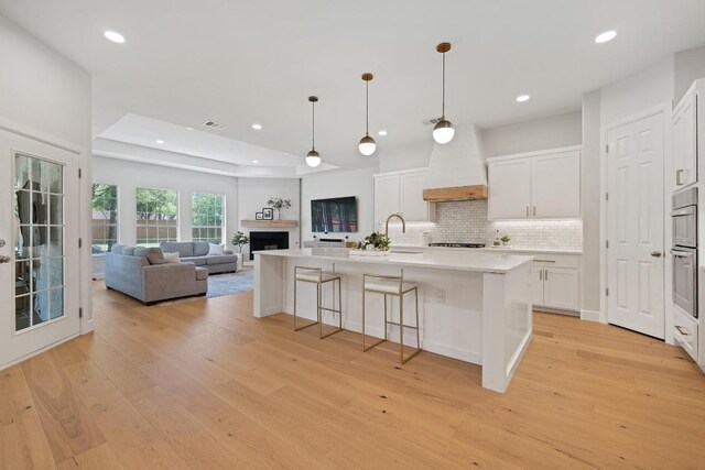113 Oak Plaza Dr, Georgetown, TX 78628 - kitchen featuring custom range hood, light wood-style flooring, cooktop, tasteful backsplash, and light countertops