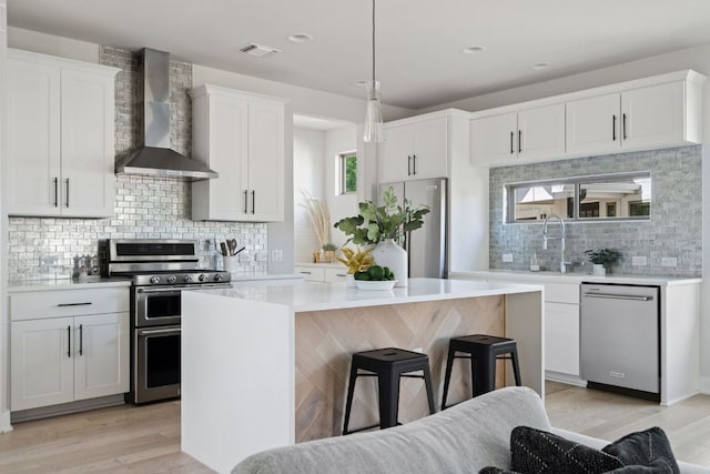 kitchen with wall chimney exhaust hood, stainless steel appliances, decorative backsplash, a kitchen island, and white cabinetry