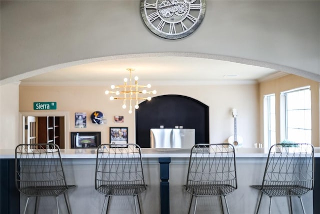 kitchen featuring a kitchen bar, open floor plan, crown molding, arched walkways, and a chandelier