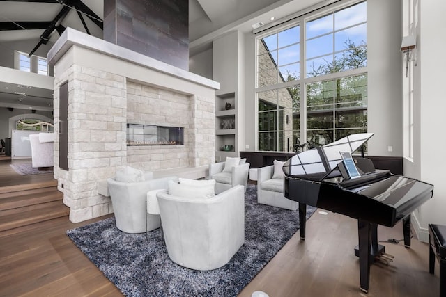 living area with a fireplace, wood finished floors, a high ceiling, and built in shelves