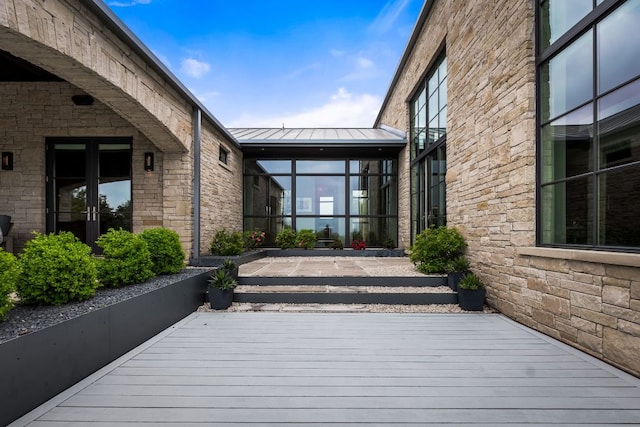 doorway to property featuring stone siding, a wooden deck, a standing seam roof, and metal roof