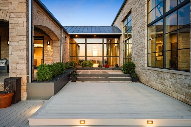 view of exterior entry with stone siding, a standing seam roof, metal roof, and a deck