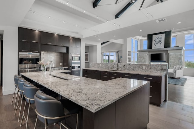 kitchen featuring backsplash, modern cabinets, a sink, a spacious island, and light wood-style flooring