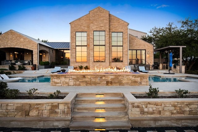 back of house featuring an outdoor pool, an outdoor fire pit, a patio area, and metal roof