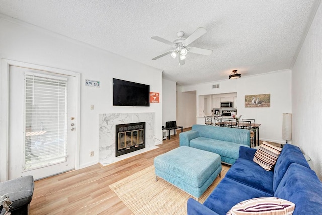 living area featuring visible vents, ceiling fan, a fireplace, a textured ceiling, and wood finished floors