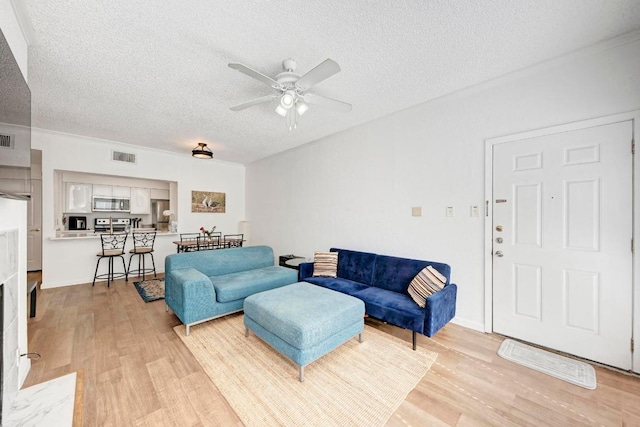 living room featuring light wood finished floors, visible vents, a textured ceiling, and ceiling fan