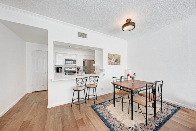 dining room featuring light wood-style floors, visible vents, and a textured ceiling