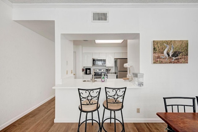 kitchen featuring a peninsula, white cabinetry, visible vents, wood finished floors, and stainless steel appliances