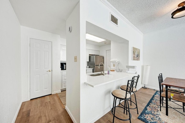 kitchen with freestanding refrigerator, white cabinets, light wood-style floors, visible vents, and a breakfast bar area