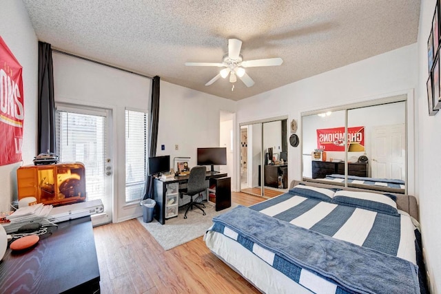 bedroom with a textured ceiling, two closets, access to exterior, ceiling fan, and wood finished floors