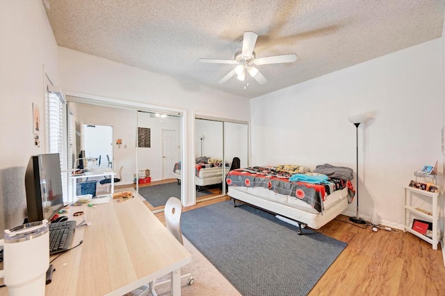 bedroom with a textured ceiling, wood finished floors, ceiling fan, and multiple closets