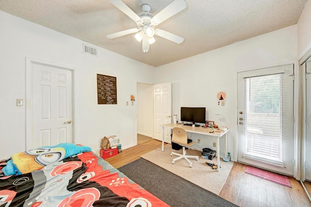 bedroom featuring visible vents, a ceiling fan, a textured ceiling, wood finished floors, and access to exterior