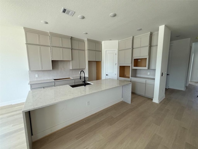 12009 Cearley Dr, Austin, TX 78758 - kitchen with a large island, tasteful backsplash, light wood-style flooring, a textured ceiling, and light stone countertops