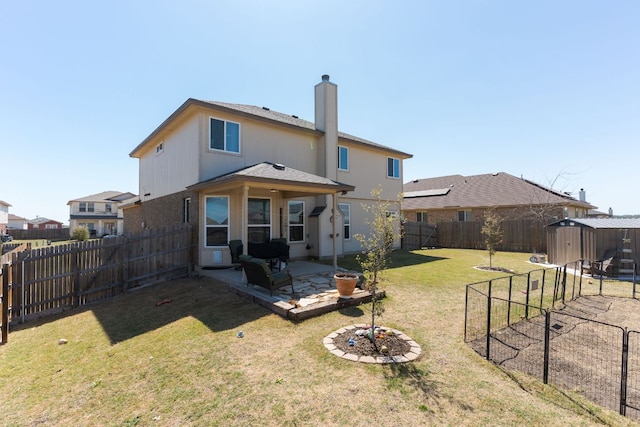 rear view of property with a yard, a chimney, a fenced backyard, an outdoor structure, and a patio