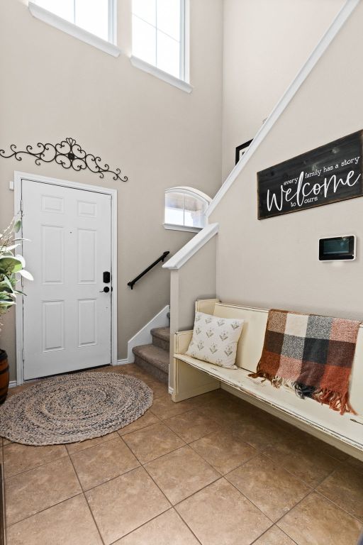 foyer entrance with light tile patterned floors, stairs, a towering ceiling, and a healthy amount of sunlight