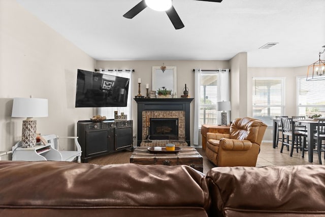living area featuring tile patterned floors, a stone fireplace, ceiling fan with notable chandelier, and visible vents