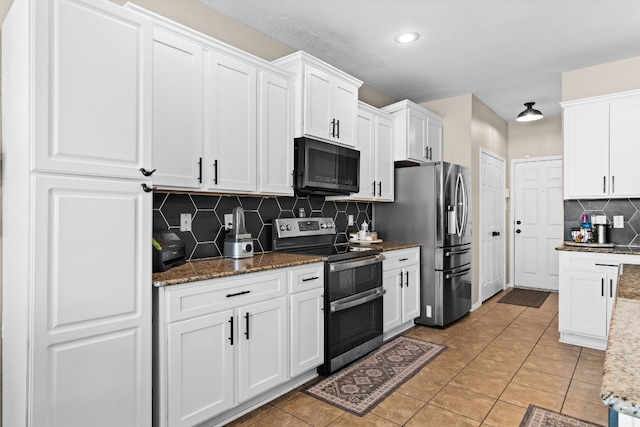 kitchen with light tile patterned floors, white cabinetry, dark stone countertops, appliances with stainless steel finishes, and backsplash