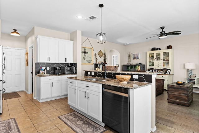 kitchen with ceiling fan, arched walkways, visible vents, a kitchen island with sink, and a sink