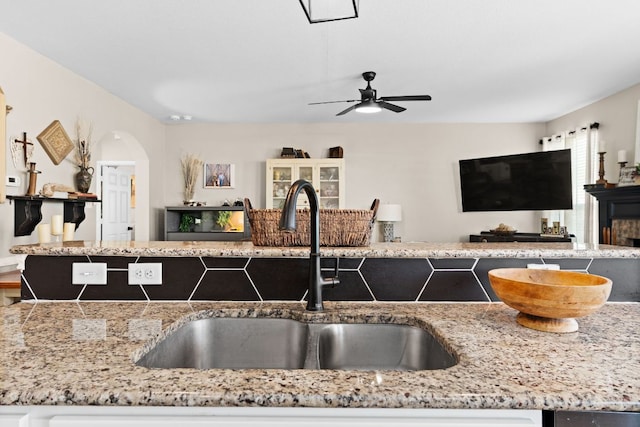 kitchen with open floor plan, a ceiling fan, light stone countertops, arched walkways, and a sink