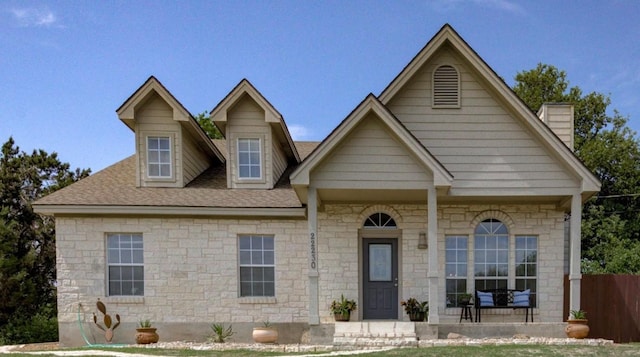 view of front of property with a chimney, roof with shingles, fence, and stone siding