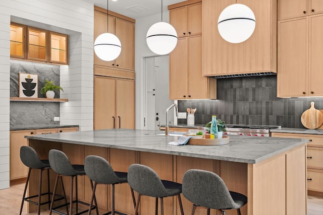 kitchen featuring tasteful backsplash, open shelves, light stone countertops, a kitchen bar, and a sink