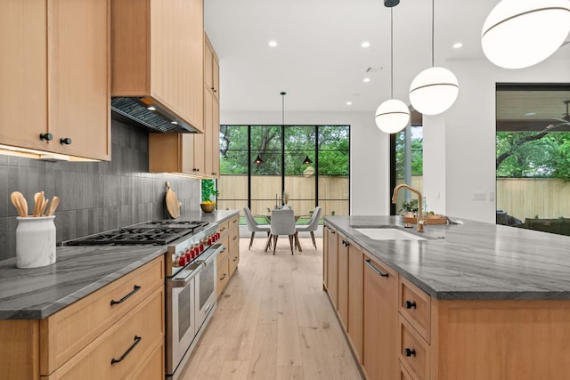 kitchen featuring light wood-type flooring, backsplash, dark stone counters, double oven range, and a sink