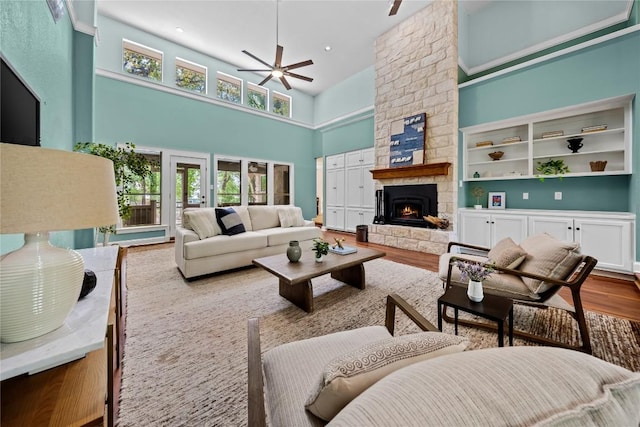 living room with a fireplace, a towering ceiling, wood finished floors, and ceiling fan