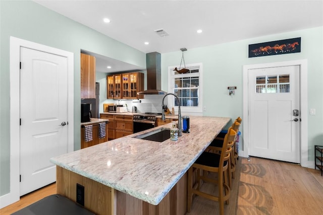 kitchen featuring wall chimney range hood, light wood-style floors, a sink, and stainless steel microwave