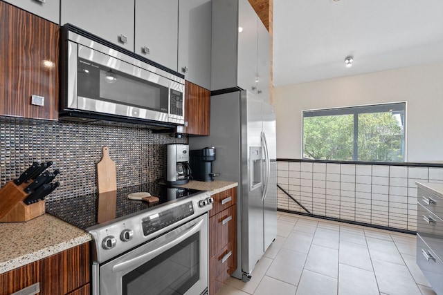 kitchen with a wainscoted wall, light tile patterned flooring, tile walls, light stone countertops, and appliances with stainless steel finishes
