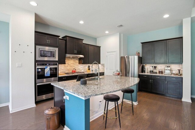 kitchen with a sink, visible vents, backsplash, under cabinet range hood, and appliances with stainless steel finishes