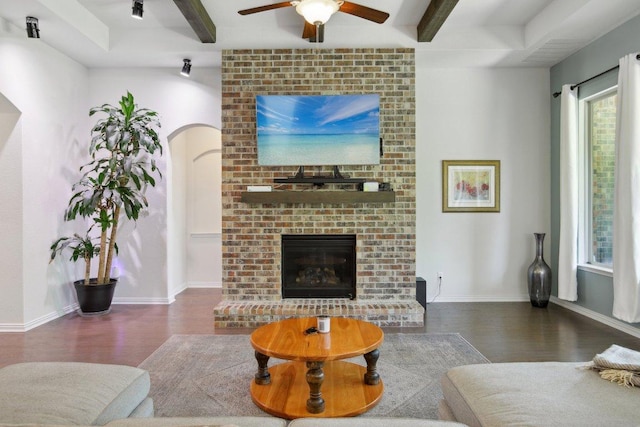 living area featuring arched walkways, beamed ceiling, wood finished floors, ceiling fan, and a fireplace