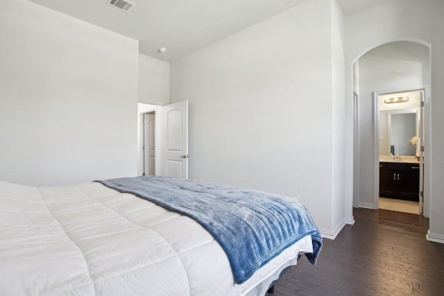 bedroom featuring vaulted ceiling, wood finished floors, arched walkways, baseboards, and visible vents