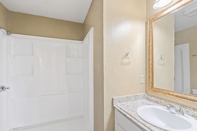 bathroom with a textured ceiling, vanity, a shower, and visible vents