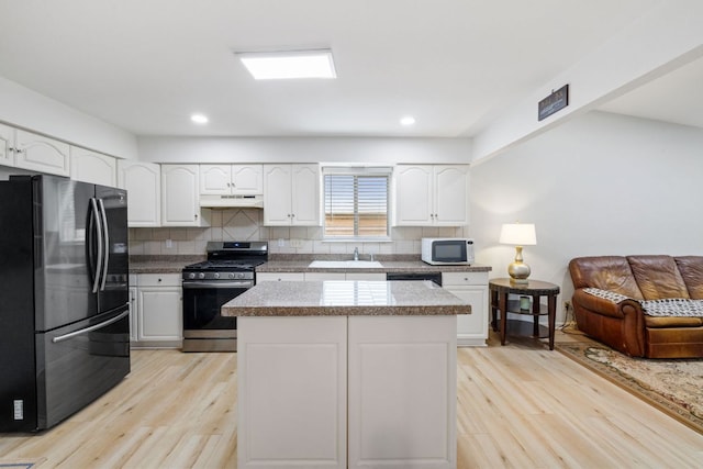 607 Elderberry Cv, Austin, TX 78745 - kitchen with freestanding refrigerator, white microwave, stainless steel range with gas stovetop, under cabinet range hood, and light wood-style floors