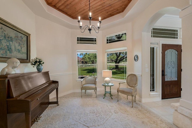 living area with tile patterned floors, a raised ceiling, wooden ceiling, arched walkways, and a notable chandelier