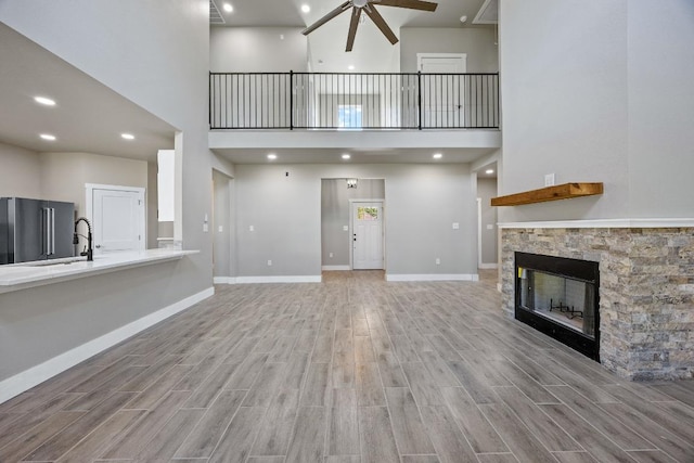 7 Harmony Ln, Wimberley, TX 78676 - unfurnished living room featuring a ceiling fan, a towering ceiling, wood finished floors, and a stone fireplace