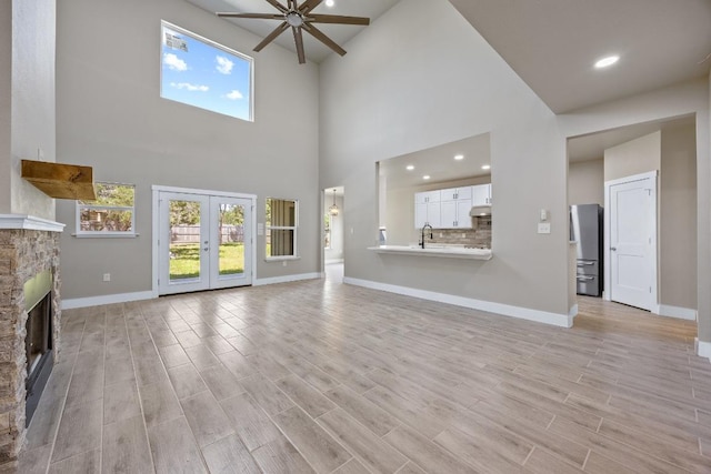 7 Harmony Ln, Wimberley, TX 78676 - unfurnished living room featuring ceiling fan, plenty of natural light, a high ceiling, a stone fireplace, and light wood-style floors