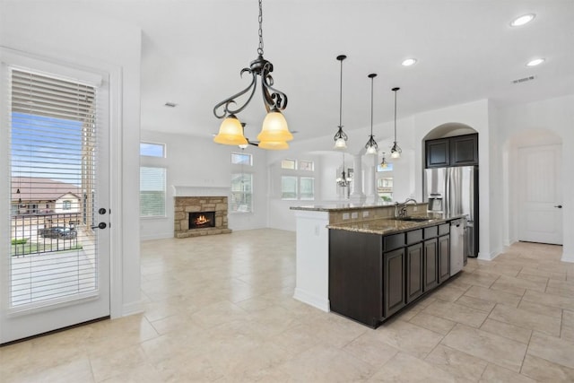 111 Antonio Way Unit 5A, Austin, TX 78734 - kitchen featuring arched walkways, stainless steel appliances, light stone counters, open floor plan, and a center island with sink