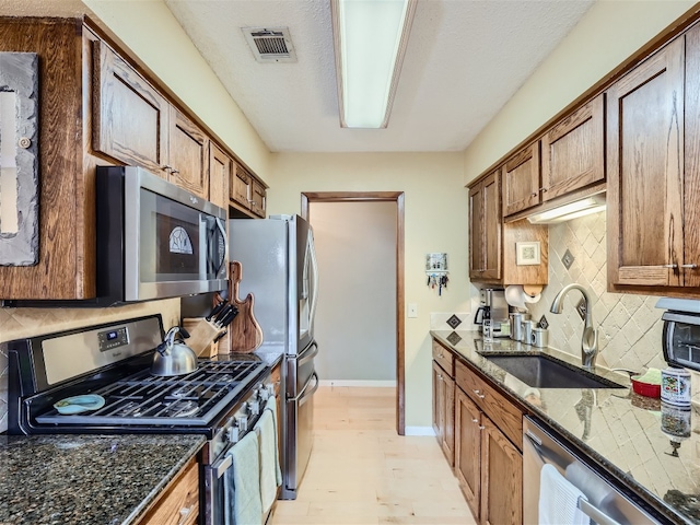 822 Hermitage Dr, Austin, TX 78753 - kitchen with appliances with stainless steel finishes, a sink, decorative backsplash, light wood-style floors, and dark stone counters