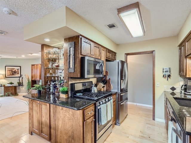822 Hermitage Dr, Austin, TX 78753 - kitchen with stainless steel appliances, light wood-style flooring, dark stone countertops, brown cabinetry, and a textured ceiling
