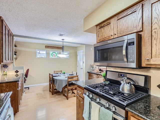 822 Hermitage Dr, Austin, TX 78753 - kitchen featuring appliances with stainless steel finishes, brown cabinets, light wood finished floors, decorative light fixtures, and a textured ceiling