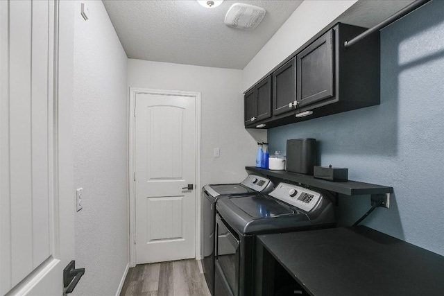 clothes washing area with wood finished floors, baseboards, washer and dryer, cabinet space, and a textured ceiling