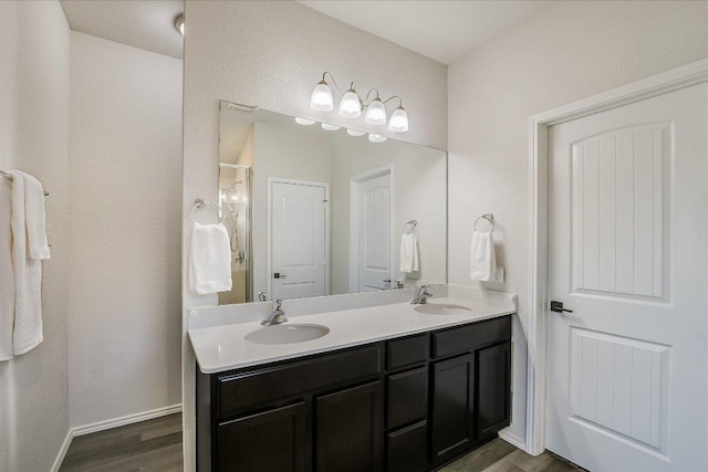 bathroom featuring wood finished floors, a sink, double vanity, and an enclosed shower