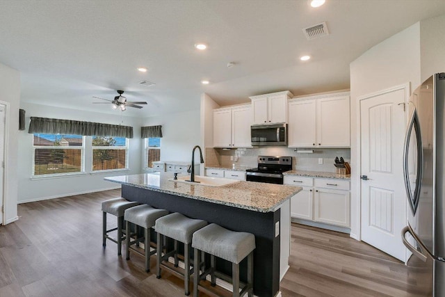 kitchen with white cabinets, a sink, backsplash, wood finished floors, and appliances with stainless steel finishes
