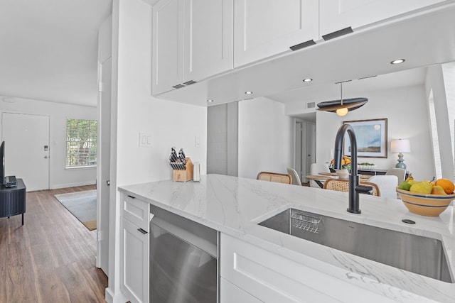 kitchen with wood finished floors, a sink, white cabinets, light stone countertops, and recessed lighting
