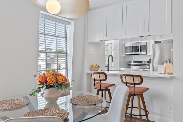kitchen with stainless steel appliances, a kitchen breakfast bar, a sink, white cabinetry, and light countertops